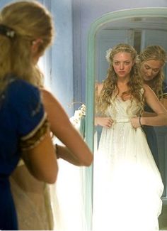 a woman standing in front of a mirror looking at her reflection wearing a wedding dress