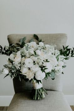 a bouquet of white flowers sitting on top of a gray chair next to a wall