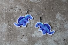 a pair of beaded dinosaur earrings sitting on top of a stone floor next to each other