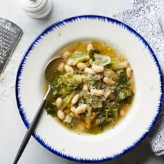 a white bowl filled with beans and greens on top of a blue and white plate