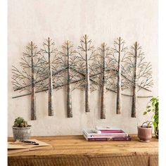 a wooden table topped with books and plants next to a wall mounted metal tree sculpture