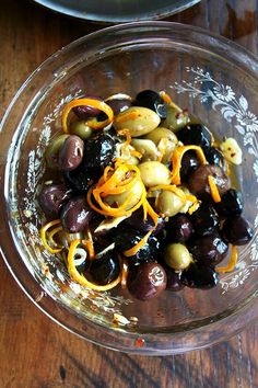 a glass bowl filled with olives and orange peels