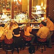 a group of people sitting at bar stools in front of a counter with liquor bottles on it