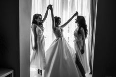 three women standing in front of a window with their arms up and one woman wearing a dress