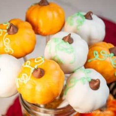 small pumpkins decorated with white and green icing are in a glass jar on a table