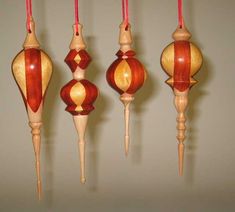 four wooden ornaments hanging from strings in a row with red string attached to each ornament