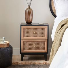 a nightstand with two drawers and a vase on it next to a black footstool