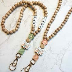 two wooden beaded lanyards with name tags and flower charms on them, sitting on a marble surface