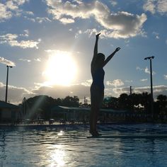 a woman standing on the edge of a swimming pool with her arms in the air