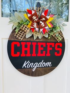 a sign that says chiefs kingdom hanging on a door with flowers and footballs painted on it