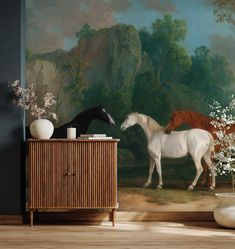 two horses standing in front of a painting on the wall next to a cabinet with vases