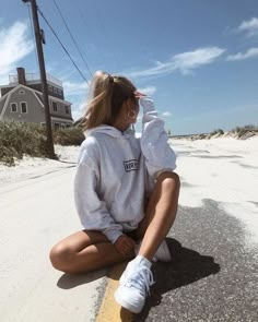 a woman sitting on the ground wearing a white hoodie and sneakers with her hands in her hair