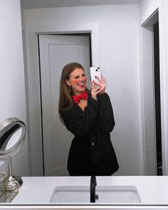 a woman taking a selfie in front of a bathroom mirror wearing a red bow tie