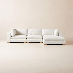 a white couch sitting on top of a floor next to a wooden frame chair and ottoman