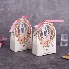 two small white boxes with pink ribbon tied around the top and an image of a bride and groom on them