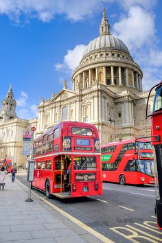 two red double decker buses parked in front of a building with a dome on top