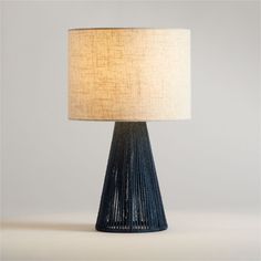 a table lamp with a white shade on the top and a blue vase underneath it