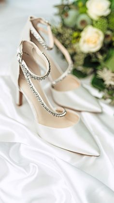 the bride's wedding shoes are sitting on her white satin bed sheet with flowers in the background