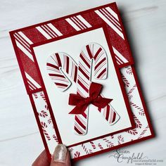 a hand holding up a card with some candy canes on it and a red bow