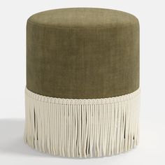 a green and white ottoman with tassels on the bottom, in front of a white background