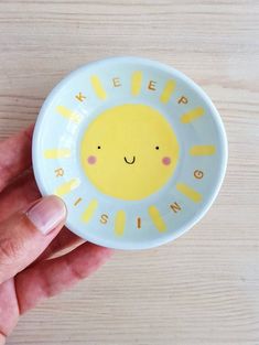 a hand holding a yellow and white bowl with a smiley face on it that says keep rising