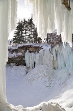 an ice cave with icicles hanging from it's sides and trees in the background