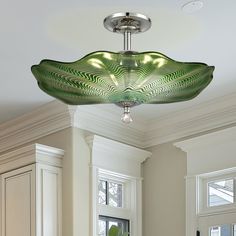 a large green glass bowl hanging from the ceiling in a room with white cabinets and windows