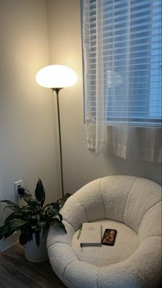 a white chair sitting in front of a window next to a lamp and a potted plant