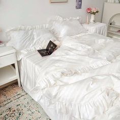 there is a white bed with ruffles on it and a book in the middle