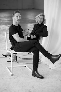 a man and woman sitting next to each other on a chair in front of a curtain