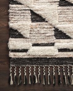 a black and white rug with tassels on top of wooden floor next to wall