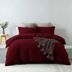 a bed with red comforter and pillows in a white room next to a plant