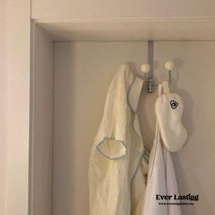 two towels hanging from hooks in a white cabinet with the words everlasting written on it