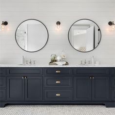 a bathroom with two round mirrors above the sinks and dark blue cabinetry on the wall