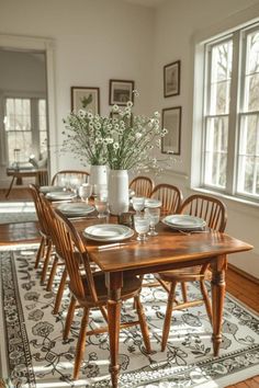 a dining room table set with place settings and flowers in a vase on top of the table