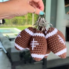 a hand holding two crocheted keychains that have footballs on them