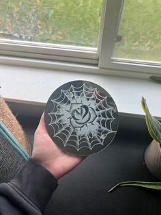 a person holding a spider web coaster in their hand next to a plant and window