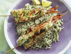 a plate with rice and chicken skewers on top of it next to lemon wedges