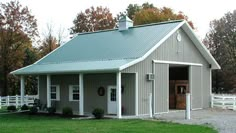 a gray barn with a green roof and white fenced in area next to it