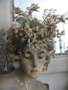 a statue with flowers on it's head in front of a mirror and window