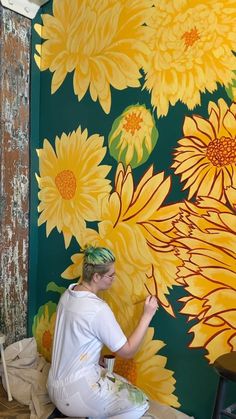 a woman sitting on the ground in front of a wall with flowers painted on it