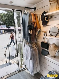 there is a woman walking by the store's clothing rack with hats on it