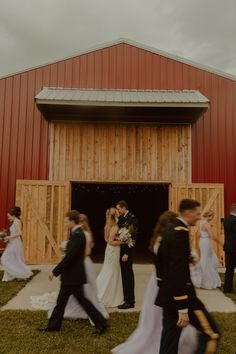 the bride and groom are walking out of the barn to their wedding party in front of them