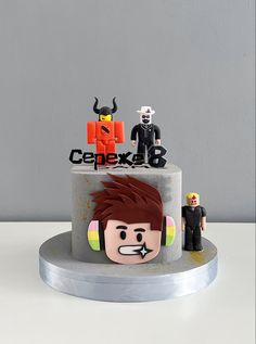 a cake decorated with legos and characters is shown on a table in front of a gray wall