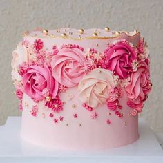 a pink and gold decorated cake with flowers on the top is sitting on a table