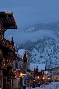 the town is decorated for christmas with lights and snow on the mountains in the background