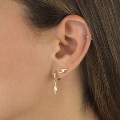 a close up of a woman's ear wearing gold earrings with lightning bolt designs