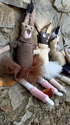 three stuffed animals sitting next to each other on a stone wall covered with leaves and rocks