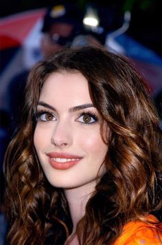 a close up of a person with long hair and blue eyeshadow wearing an orange dress