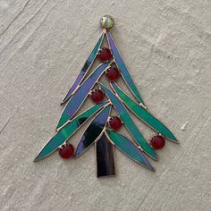 a stained glass christmas tree ornament hanging on a white surface with red beads